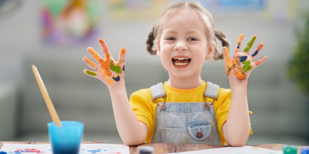 Happy kid is painting at home. The girl is being creative work sitting at the desk.